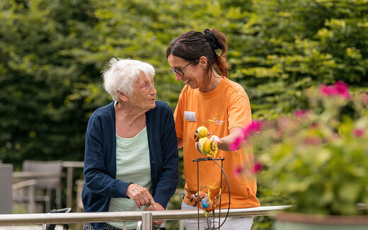 Frau geht mit älterer Dame im Garten spazieren 