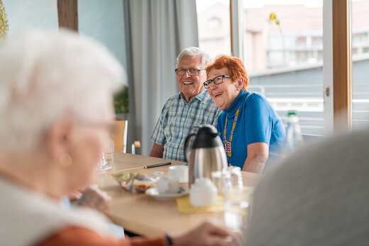 Senior und Seniorin trinken gemeinsam Kaffee mit anderen Senioren 