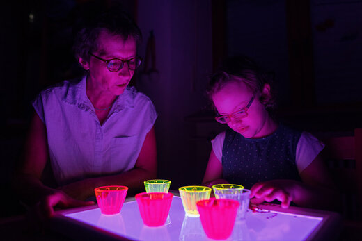 Kind mit Betreuerin in dunklem Raum mit bunten Lichtern 